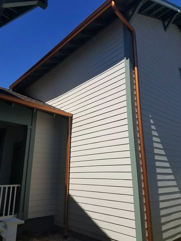 Two copper downspouts gable end cream lap siding exposed rafters, Sanford